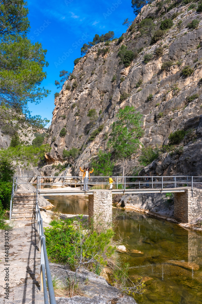 Tourists walking on bridge over canaletes river in la fontcalda sanctuary, gandesa, tarragona, spain