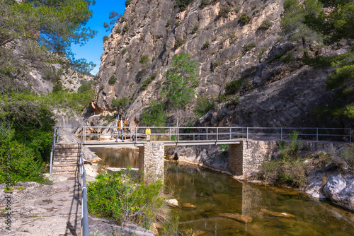 Obraz na płótnie Tourists walking on bridge over canaletes river at fontcalda sanctuary in gandesa, tarragona, spain w salonie