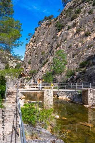 Tourists walking on bridge over canaletes river in la fontcalda sanctuary, gandesa, tarragona, spain
