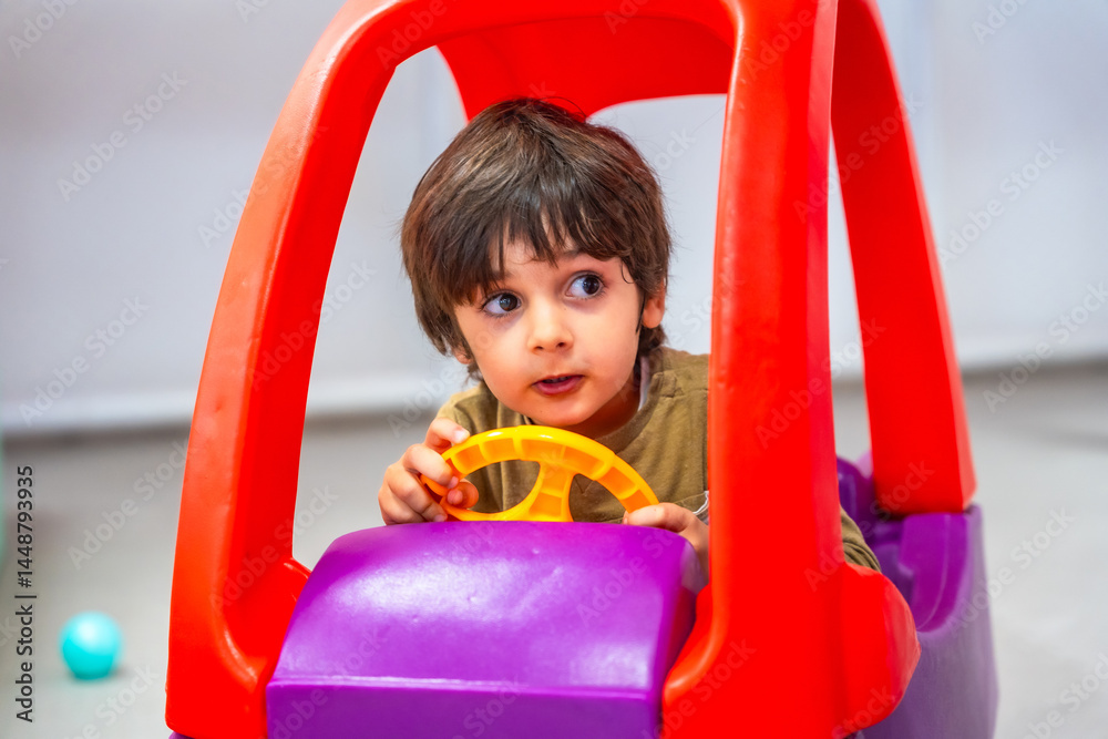 Cute child playing with toy car and steering wheel
