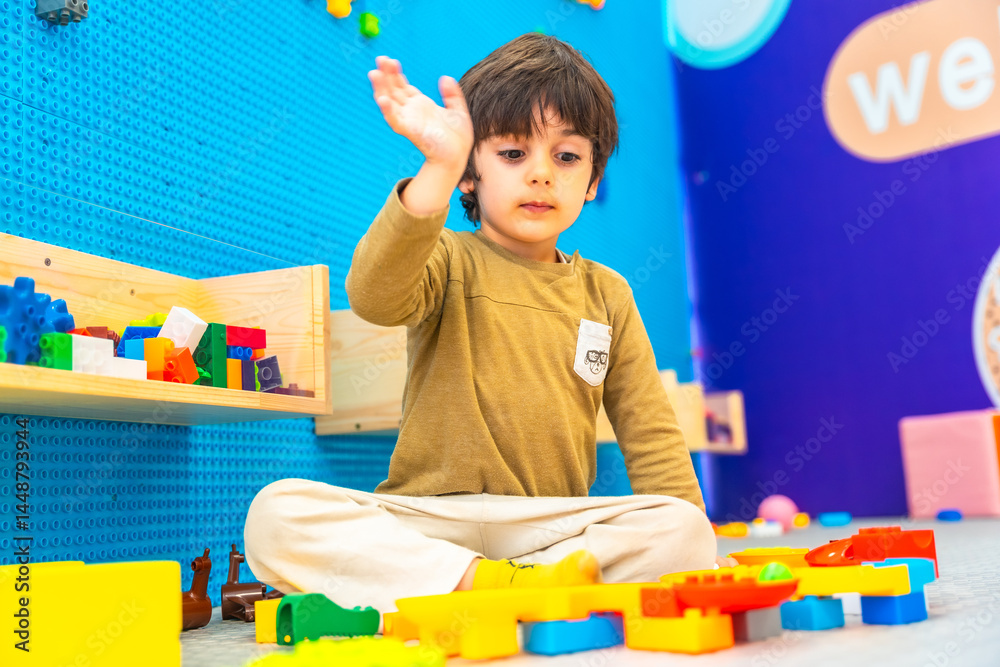 Preschooler boy playing with colorful building blocks in playroom