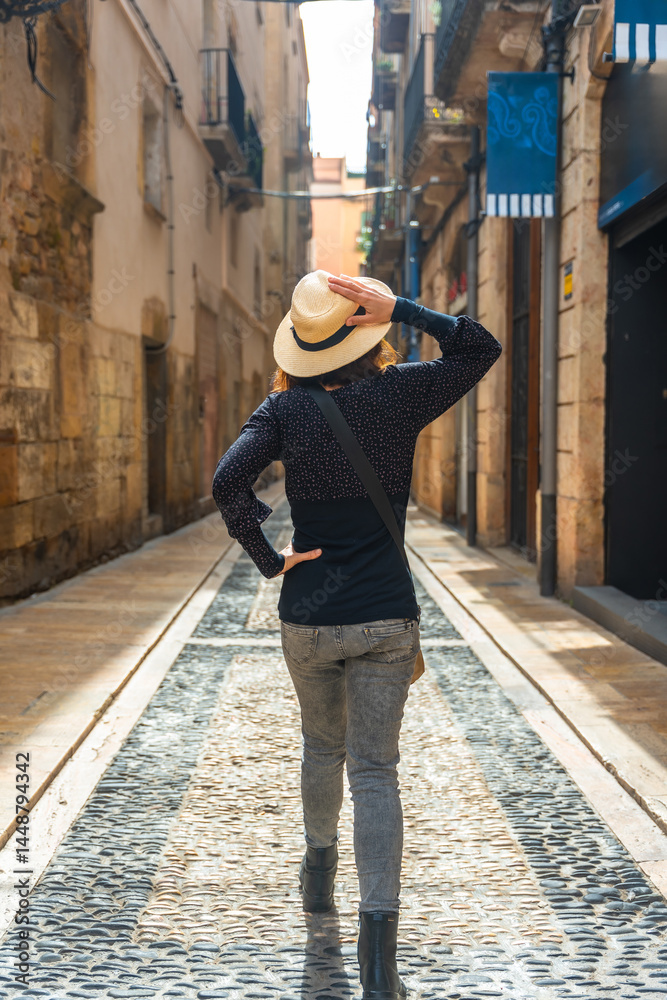 Tourist walking in medieval city of tarragona, spain, holding her hat
