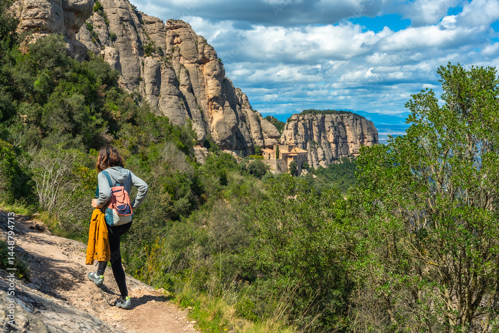 Tourist walking on a hiking trail in montserrat mountains with santa maria de montserrat monastery