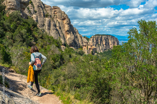 Tourist walking on a hiking trail in montserrat mountains with santa maria de montserrat monastery