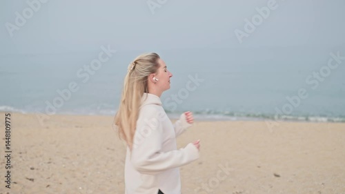 girl doing exercises and listening music in earbuds on a beach. Attractive joyful woman on a beach