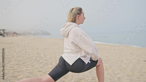 Side view young woman stretching her body on the beach. Wellness, warm up