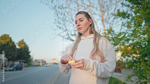 Young woman listens to music outside on a sunny day. She is wearing beige athletic wear and earbuds.