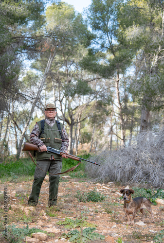 Hunter holding shotgun standing in forest with dog during hunt