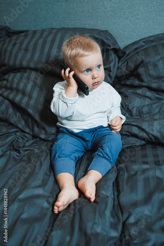 Obraz na płótnie Cute little boy 2 years old using smartphone, looking at screen, child holding phone in hands, sitting on sofa at home alone, playing game on mobile device, watching cartoons online w salonie