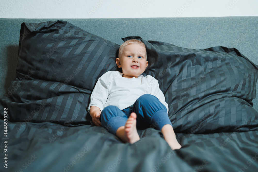 Funny 2 year old little boy wearing pajamas resting and playing in bed. Little toddler boy playing in bed.