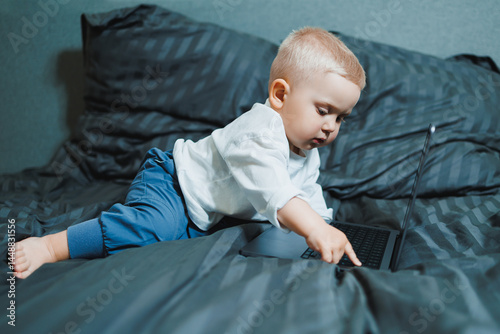 Obraz na płótnie Little boy toddler using laptop watching video at home, early education and learning. Little child looking at laptop screen and listening to music while sitting on bed. w salonie