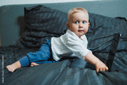 Obraz na płótnie Little boy toddler using laptop watching video at home, early education and learning. Little child looking at laptop screen and listening to music while sitting on bed. w salonie
