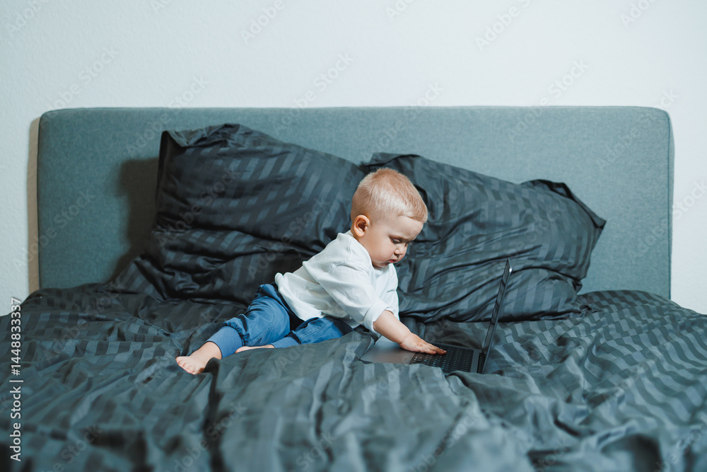 Cute little boy 2 years old sitting at home using laptop. Toddler boy watching video on laptop. Modern digitalization of children. Child watching educational videos on laptop.