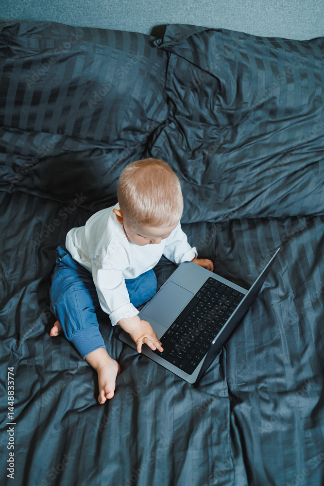 Cute little boy 2 years old sitting at home using laptop. Toddler boy watching video on laptop. Modern digitalization of children. Child watching educational videos on laptop.