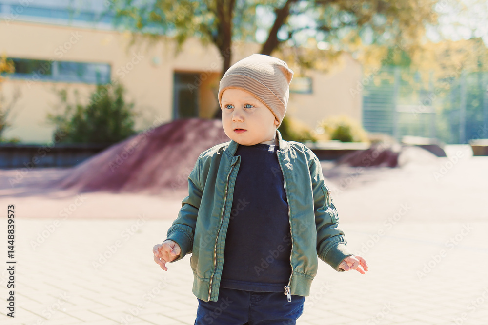 A 2 year old boy in a hat and jacket runs and plays outside. Toddler on a spring walk in the park. Child outdoors on a playground.