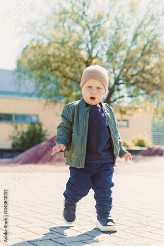 Obraz na płótnie A 2 year old boy in a hat and jacket runs and plays outside. Toddler on a spring walk in the park. Child outdoors on a playground. w salonie