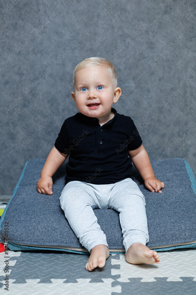 Blue-eyed blond boy 2 years old playing at home in the room. Toddler boy smiling looking at the camera. Home clothes for children.