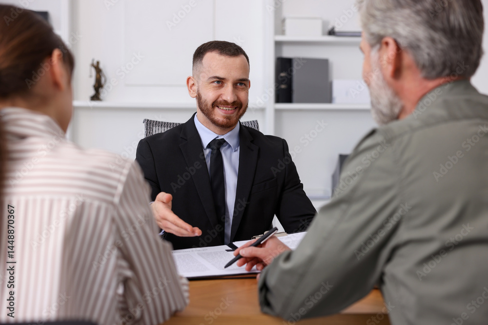 Clients signing notarial paperwork during meeting with lawyer at wooden desk indoors Clients signing notarial paperwork during meeting with lawyer at wooden desk indoors