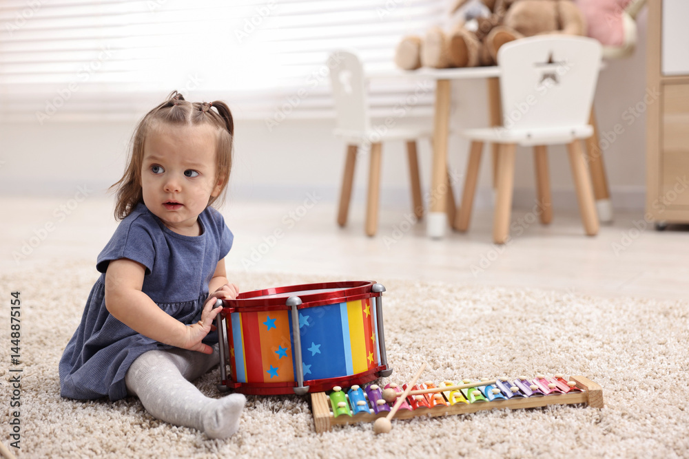 Naklejka premium Cute little girl playing with toy drum on floor at home, space for text