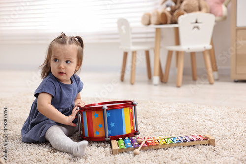 Cute little girl playing with toy drum on floor at home, space for text