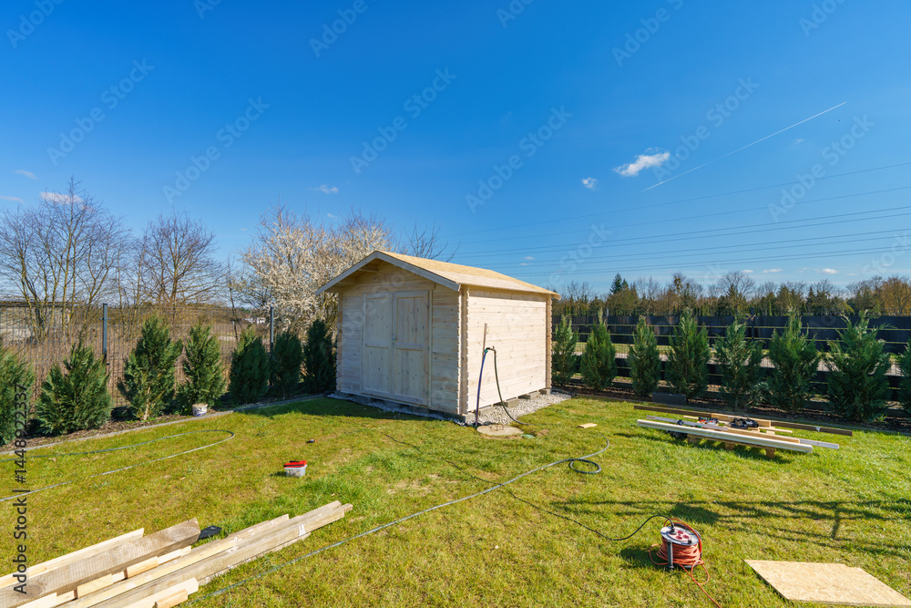 Wooden unpainted shed in the garden under clear blue sky