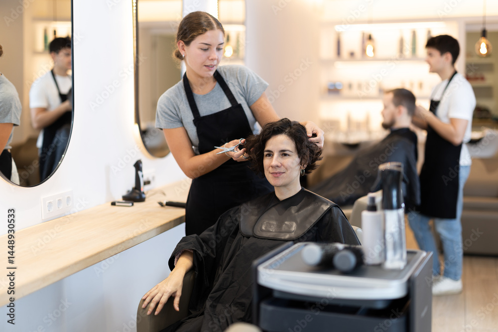 Fototapeta premium Young female hairdresser gives haircut to adult woman client in beauty salon