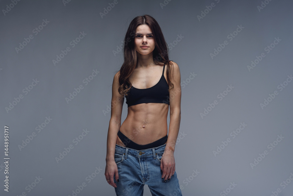 Fototapeta premium Pretty girl with perfect body and trained abs demonstrates weight loss slimming by wearing big jeans