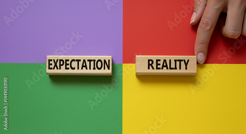 Expectation versus reality concept with wooden blocks on a colorful background and a hand touching reality