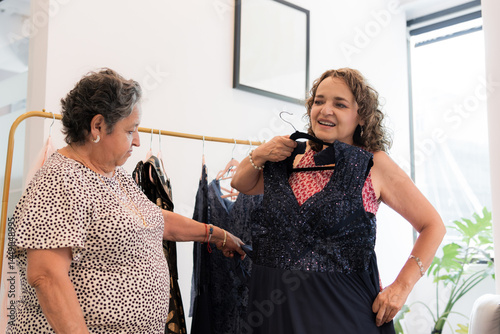 Two elderly women in a store trying on evening dresses.