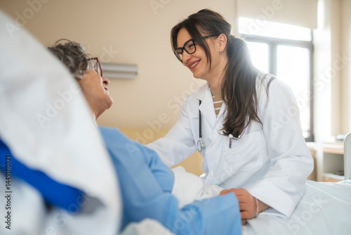 Female doctor comforting elderly patient in hospital bed