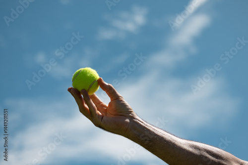 Hand holding tennis ball against blue sky background