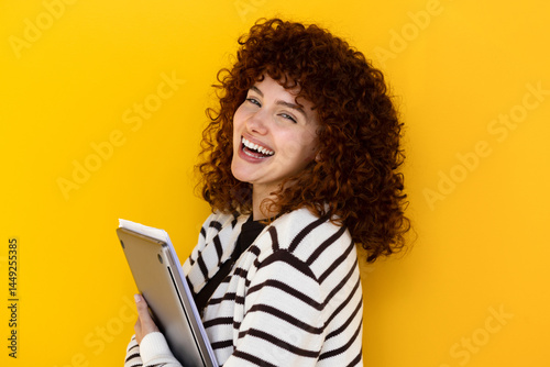 Young woman laughing while holding documents, yellow background
