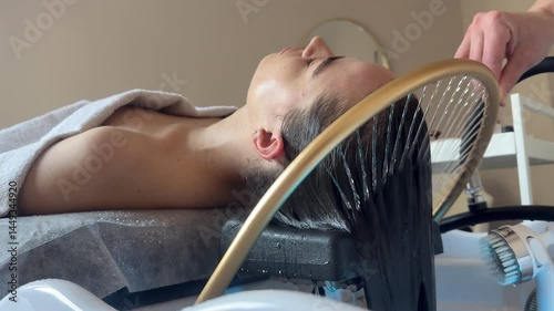 Close-up of a woman receiving a head massage during a Japanese head spa treatment with water flowing from a special hair washing tool, focusing on the scalp relaxation and beauty therapy