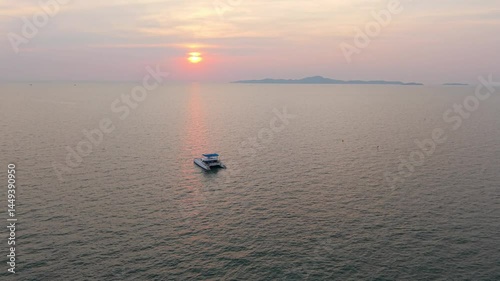 Golden hour sunlight illuminates a single boat drifting serenely on tranquil waters, creating a picturesque maritime scene with a distant island adding to the serene atmosphere