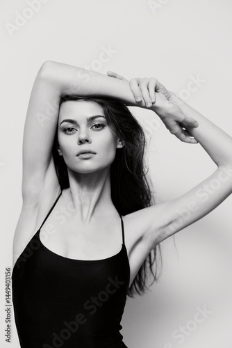 Elegant woman posing in a black sleeveless outfit against a white background, expressing confidence and grace with a soft expression.
