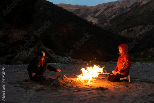 Siblings camping enjoying a fire at night, South Island, New Zealand.