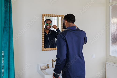 Man in stylish pajamas brushing teeth in bathroom