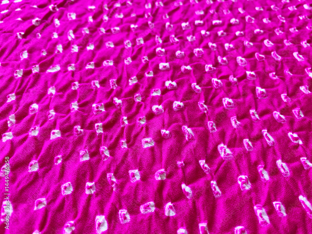 Obraz premium Tiny white Bandhani dots punctuate the pink silk fabric, creating a subtle, textured surface.