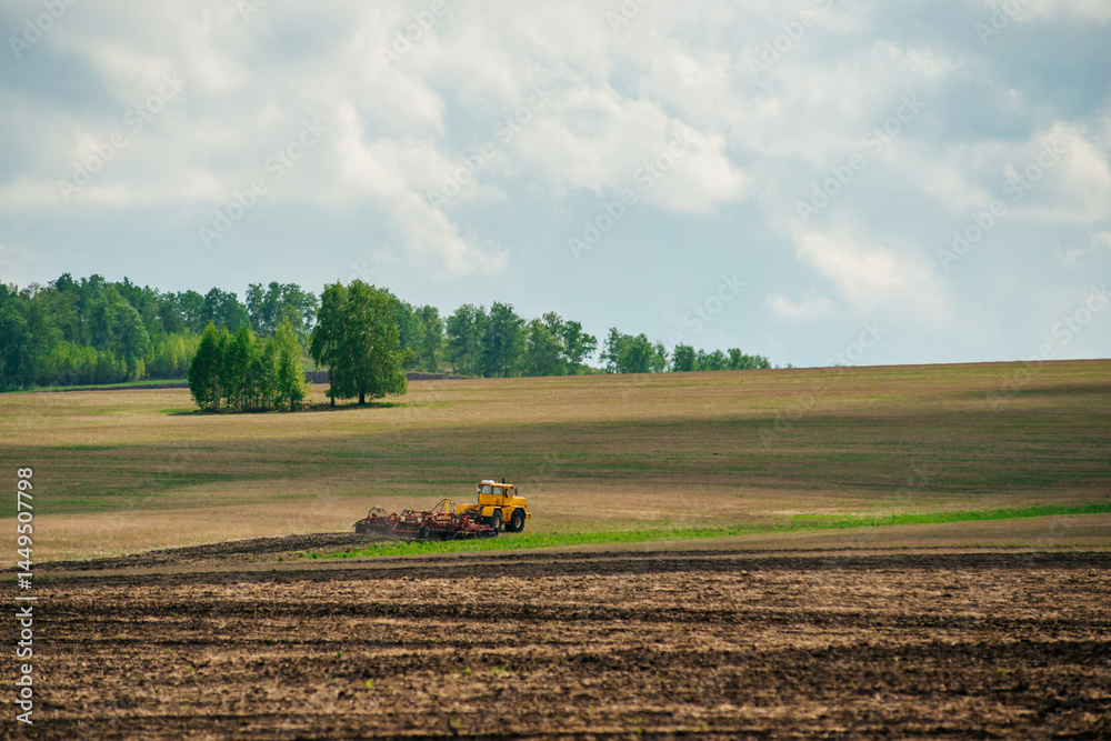 Obraz premium A yellow tractor works in a field on a farm in the spring 