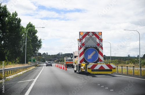 Roadwork arrow sign on back of the work truck. Orange traffic cones and unrecognizable cars driving on the road. Waikato. New Zealand.