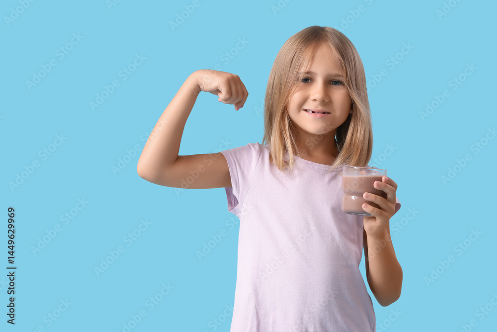Fototapeta premium Cute little girl with glass of sweet chocolate milk showing muscles on blue background