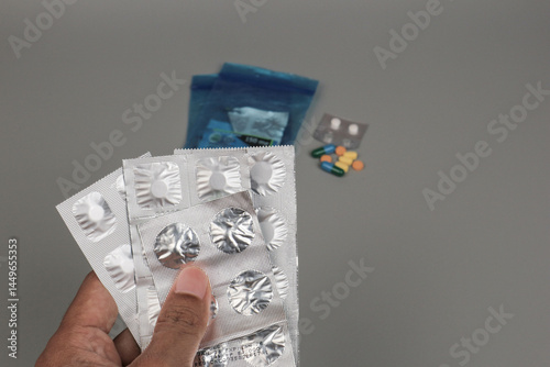 A hand holding several blister packs of medicine with scattered pills in the background, illustrating medication use, healthcare routine, or drug consumption concept.