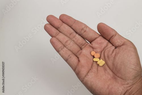 Close-up hand holding a variety of colorful pills and capsules, including round tablets on a plain background.