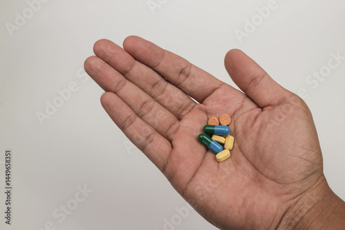 Close-up hand holding a variety of colorful pills and capsules, including round tablets on a plain background.