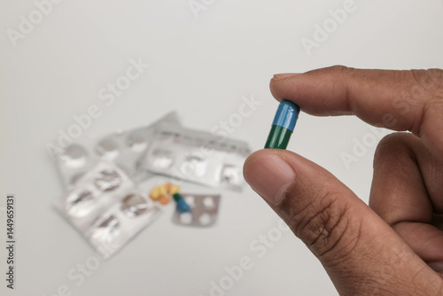 Close-up of a hand holding a single tablet with blurred medical supplies in the background