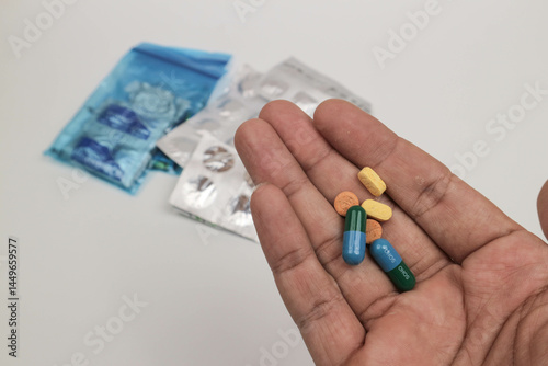 Close-up of a hand holding various pills and tablets with blurred medical supplies in the background