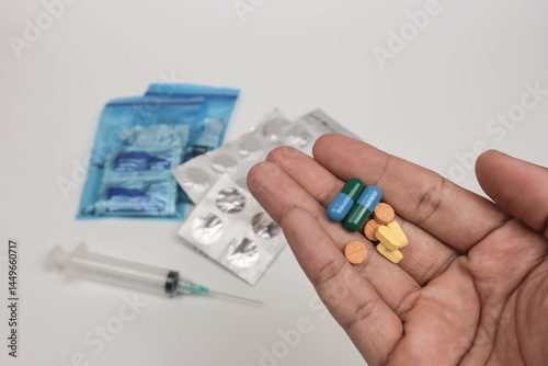 Close-up of a hand holding various pills and tablets with blurred medical supplies in the background
