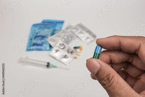 Close-up of a hand holding a single tablet with blurred medical supplies in the background