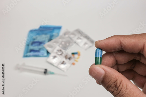 Close-up of a hand holding a single tablet with blurred medical supplies in the background