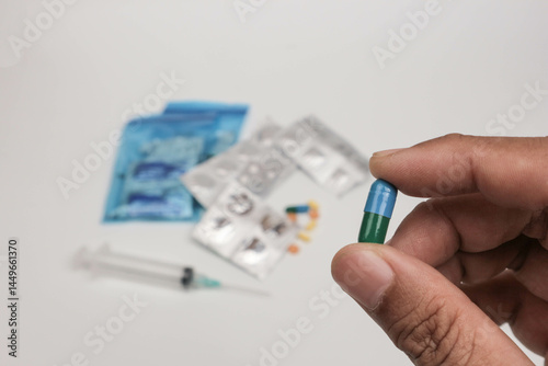 Close-up of a hand holding a single tablet with blurred medical supplies in the background